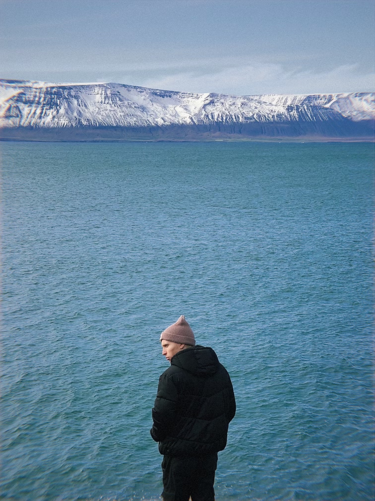 Figure beside blue water and distant mountains