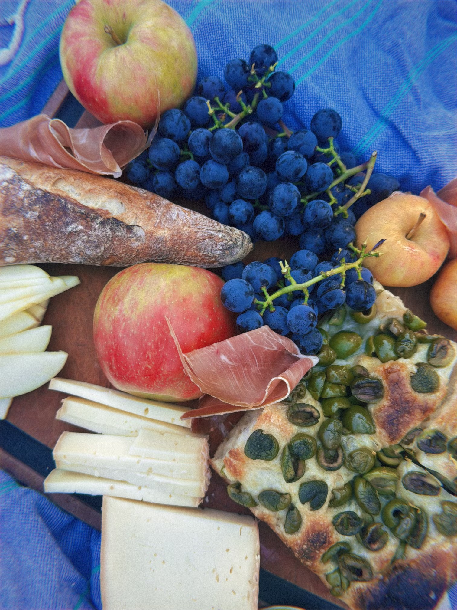 Bread, cheese, fruit, and grapes spread across a blue picnic cloth